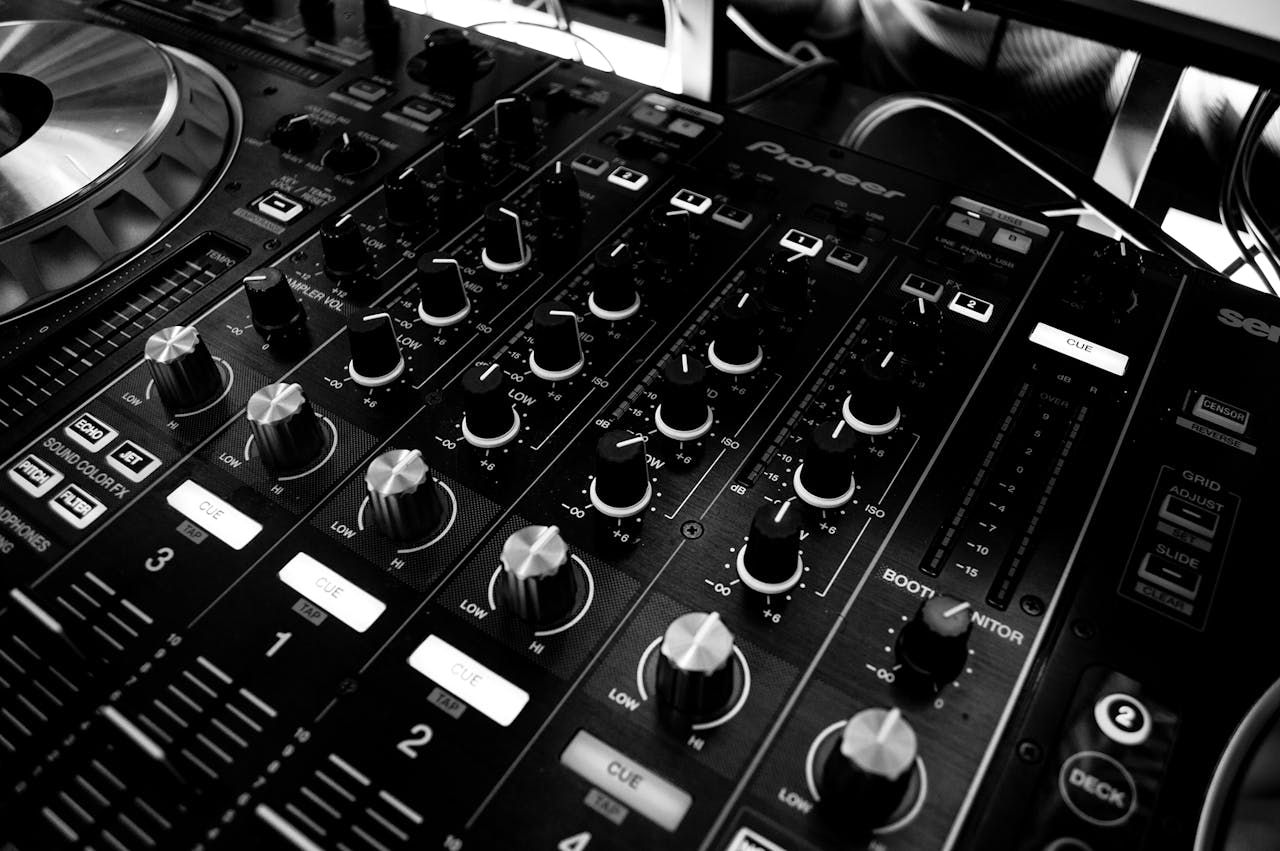 menu-01 Black and white close-up of a DJ's audio mixing console with knobs and controls.